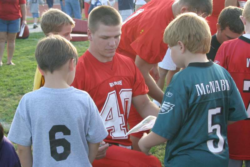a man in a football jersey reading a book with a group of kids