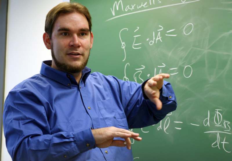 a man in a blue shirt pointing at a chalkboard