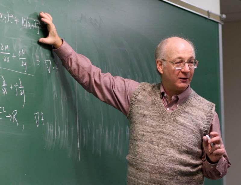 a man in a vest pointing at a chalkboard
