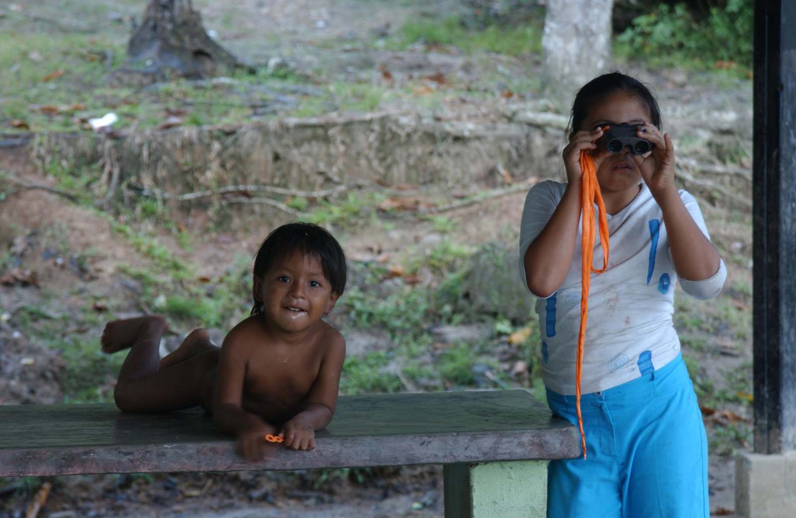 a girl looking through binoculars while a boy lying on a bench