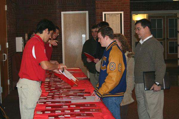 a group of people standing around a table with red folders