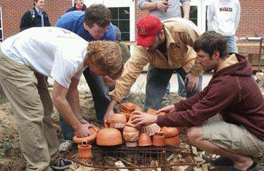 a group of men placing clay pots on a fire
