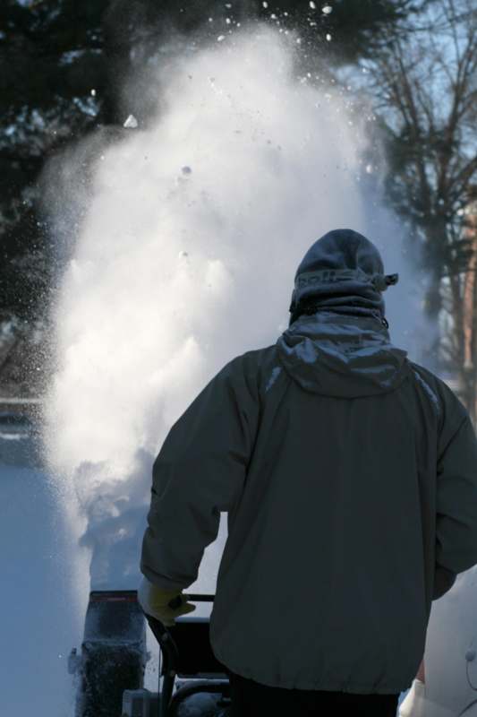 a man in a jacket and hat with a snow blower