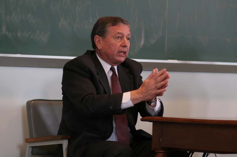 a man in a suit and tie sitting in front of a chalkboard