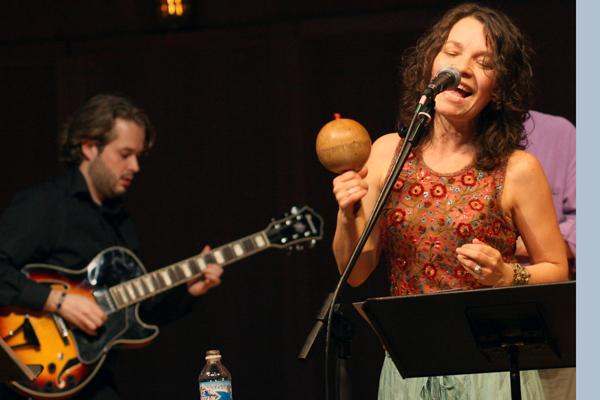 a woman singing into a microphone with a man playing guitars