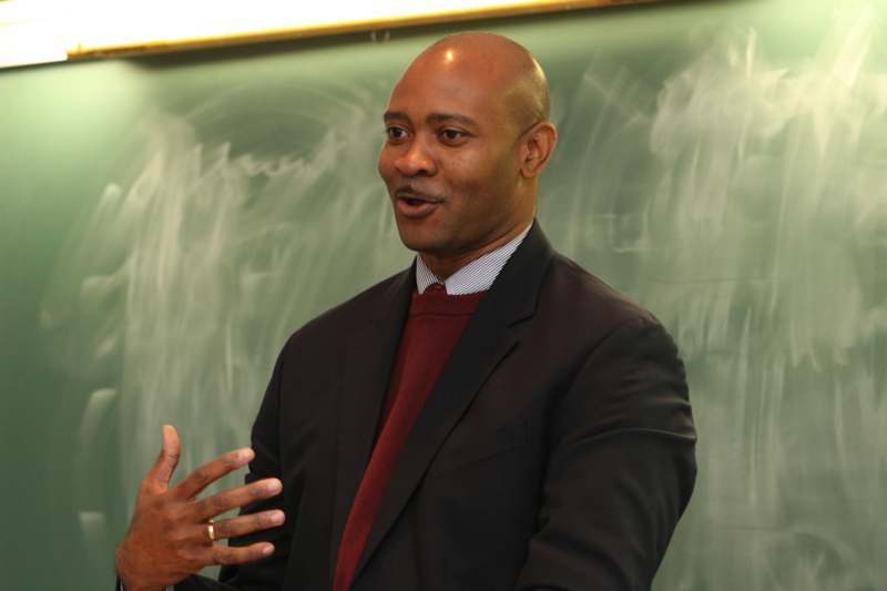a man in a suit speaking in front of a chalkboard