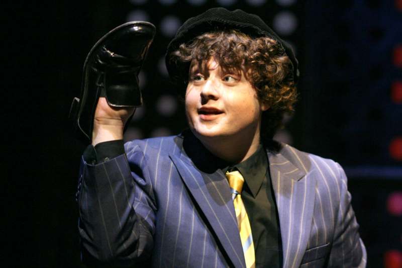 a man in a suit and hat holding a shoe up