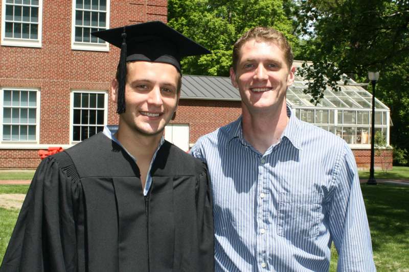a man in a graduation gown and cap standing next to a man in a cap and gown
