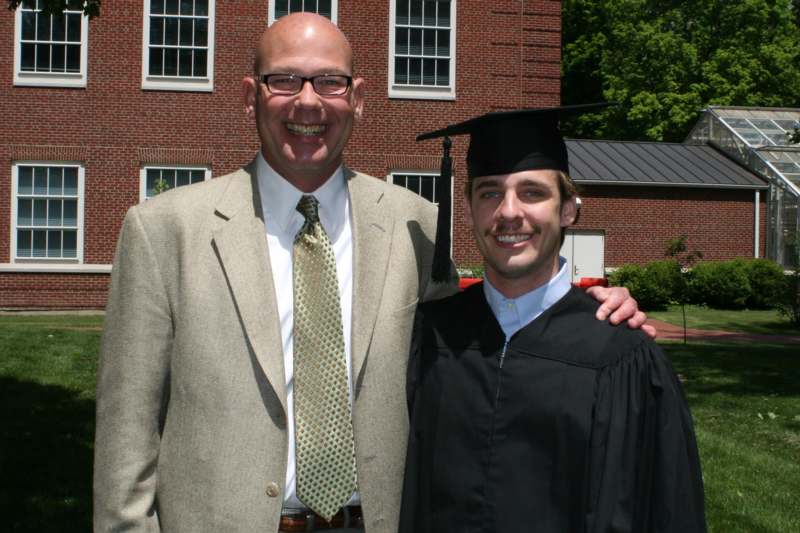a man in a suit and cap standing next to a man in a graduation gown