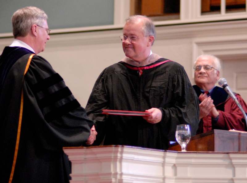 a man in a black robe shaking hands with another man in a black robe