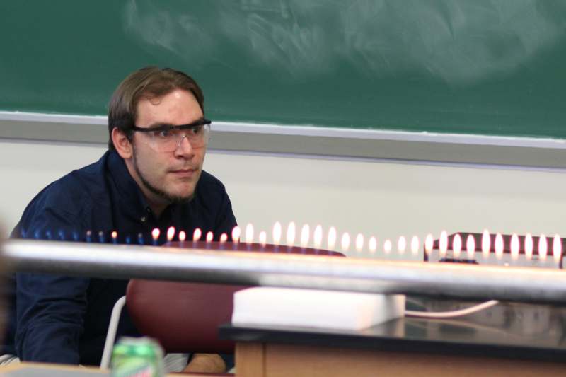 a man wearing safety goggles and standing in front of a chalkboard