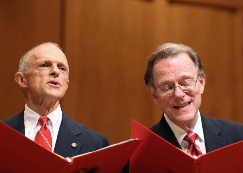 a pair of men in suits and ties reading a book