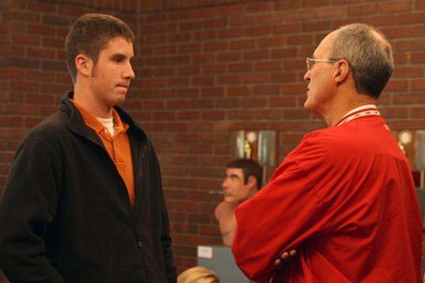 a man in a red shirt talking to a man in a black jacket