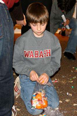 a young boy kneeling on the ground holding an orange and candy