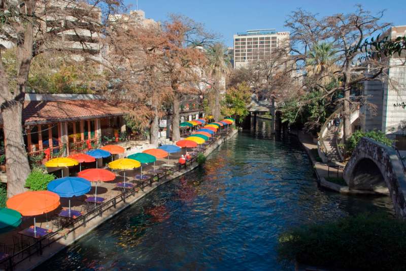 a river with colorful umbrellas with San Antonio River Walk in the background