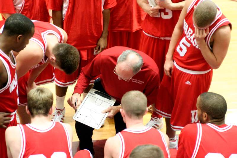 a coach writing on a clipboard while a group of men stand around