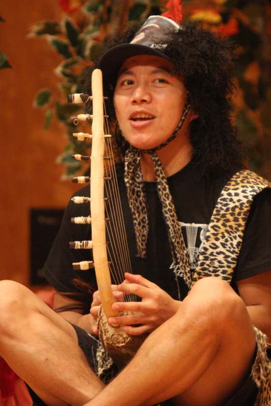 a man with a black hat and black curly hair playing a musical instrument