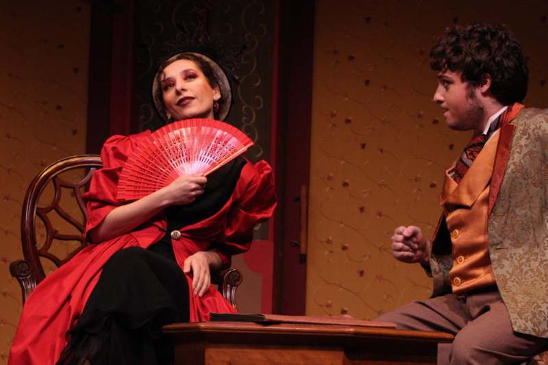 a woman holding a fan and sitting next to a man