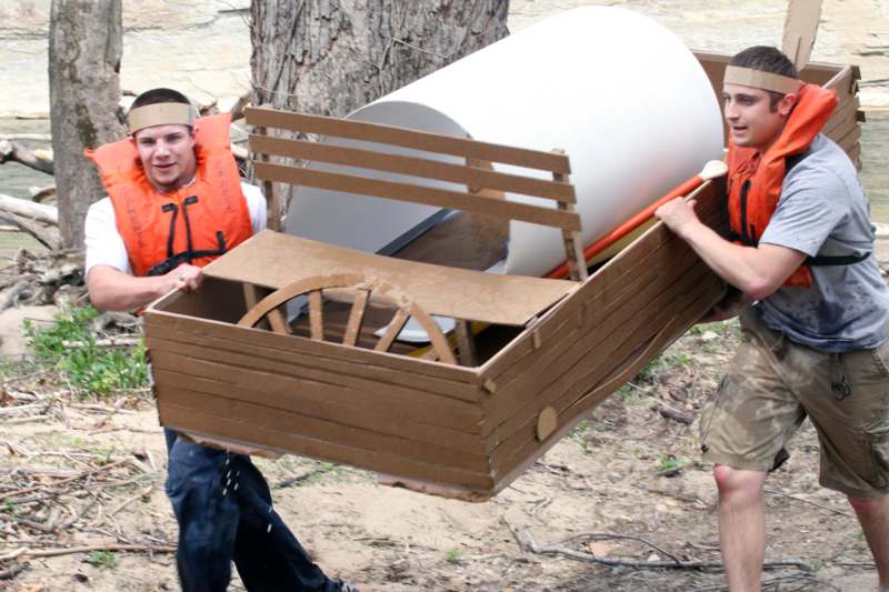 two men carrying a cardboard boat