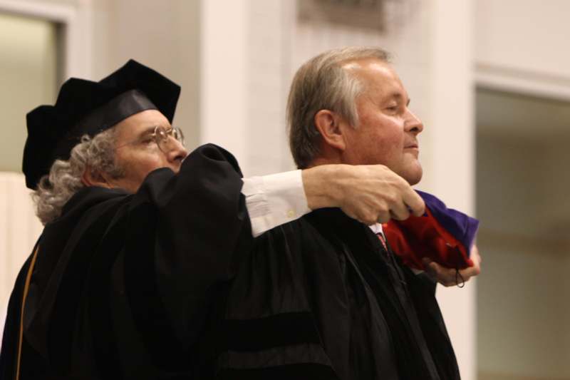 a man in a graduation gown pointing at another man