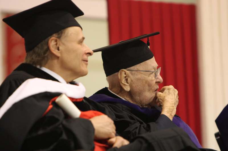 a man in a graduation gown and cap looking at another man