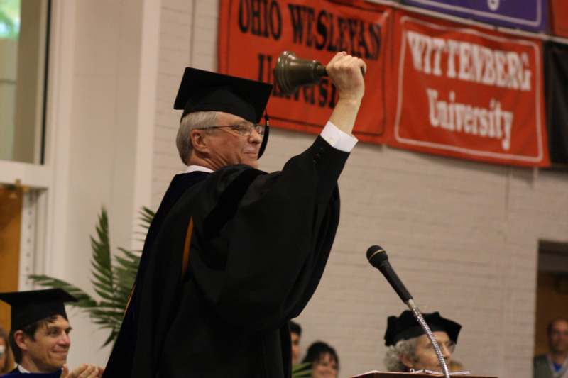 a man in a graduation gown raising a bell