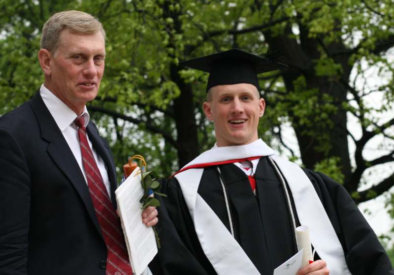 a man in a cap and gown standing next to a man in a graduation gown