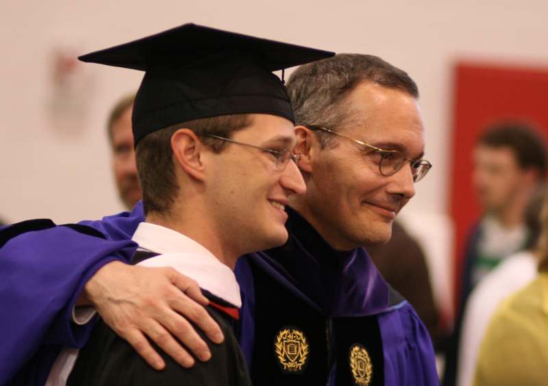 a man in a graduation gown hugging another man
