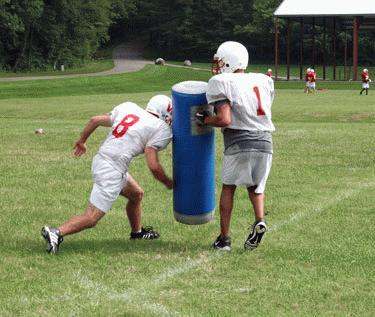 a football players pushing a large blue cylinder