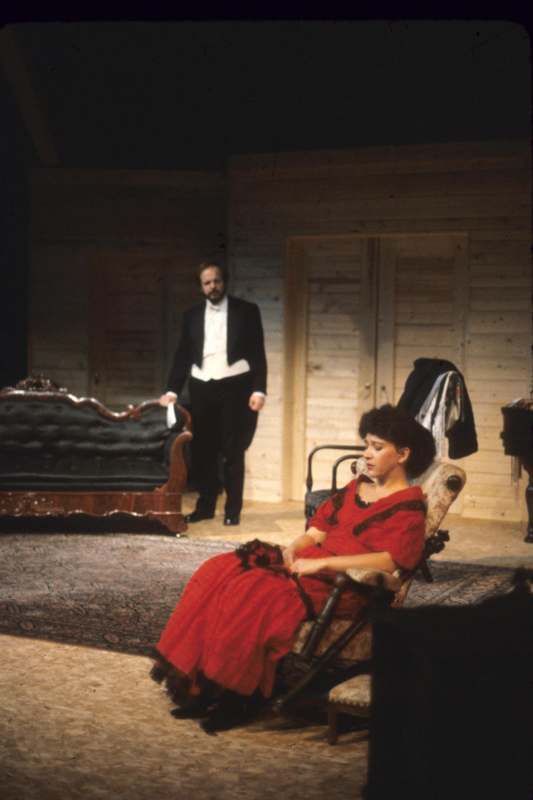 a woman in a red dress sitting in a chair in front of a man in a tuxedo