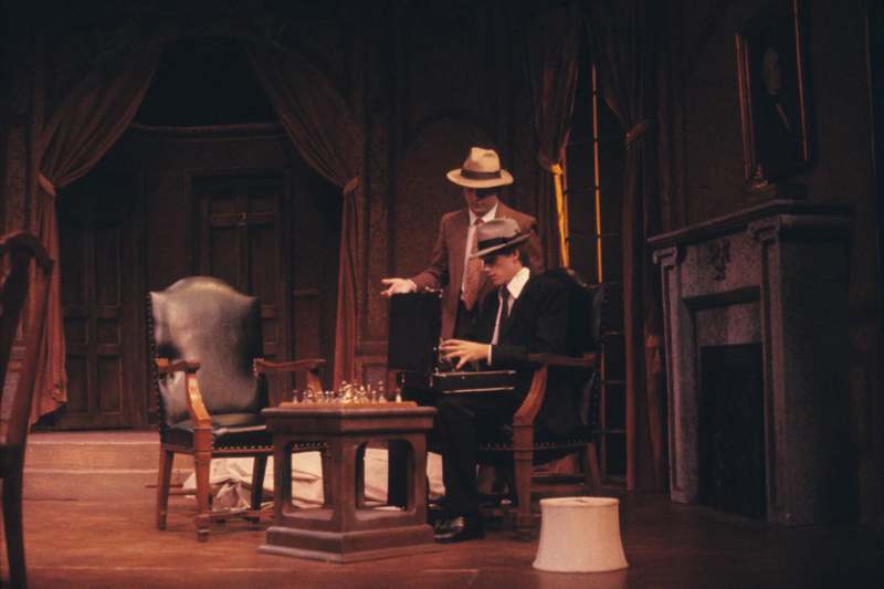a man in a suit and hat sitting in a chair with a man in a suit and hat