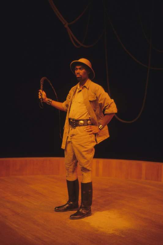 a man in safari outfit holding a whip