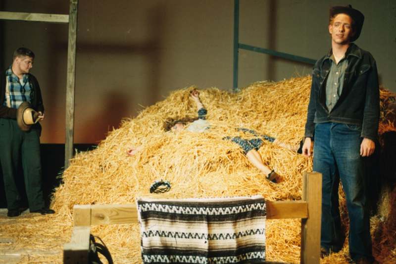 a man standing next to a woman lying in hay