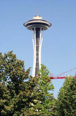 a tall tower with a crane in the background with Space Needle in the background