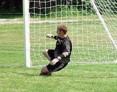 a man in a black shirt and white gloves kneeling next to a goal