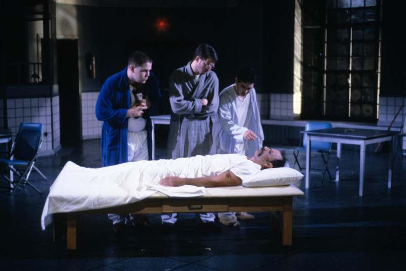 a group of men standing around a man lying on a bed