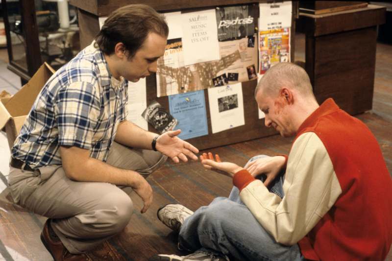 a man sitting on the floor with another man touching his hand