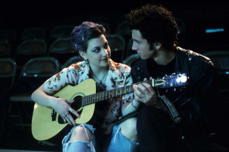 a man and woman sitting on a stage playing guitar