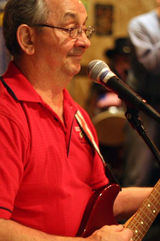 a man in a red shirt playing guitar and singing into a microphone