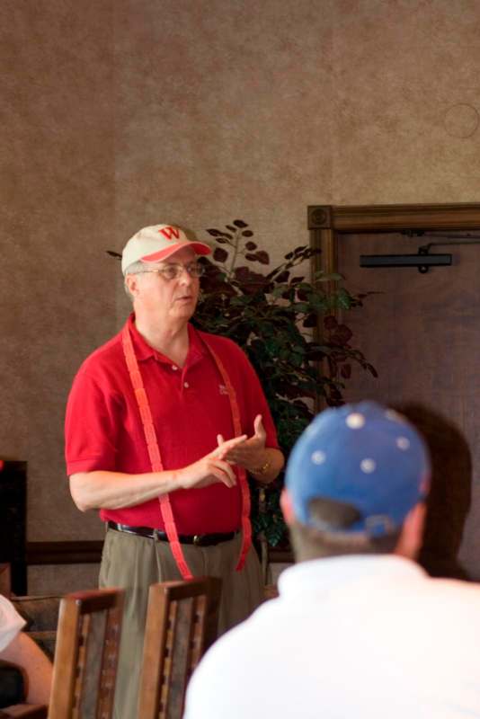 a man in a red shirt and cap speaking to a group of people
