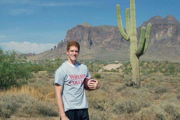 a man holding a football in front of a cactus