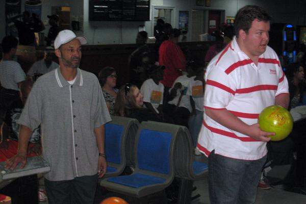 a man in a white hat standing next to another man in a bowling alley
