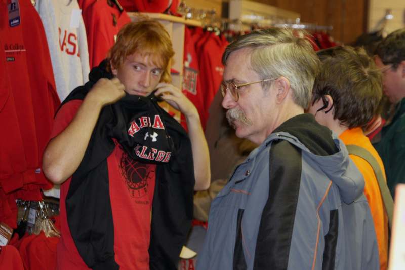 a man looking at a person holding a black and red shirt