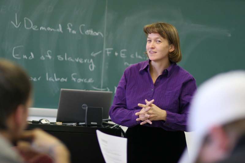 a woman in a purple shirt standing in front of a chalkboard