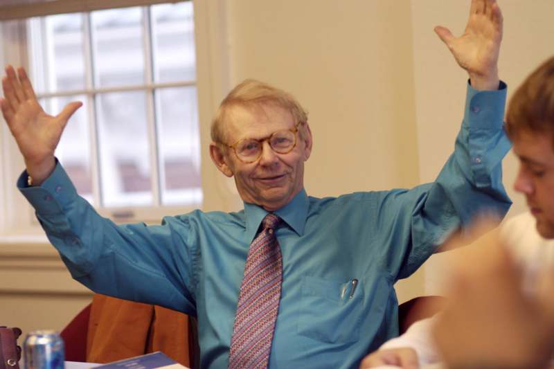a man in a blue shirt and glasses raising his hands