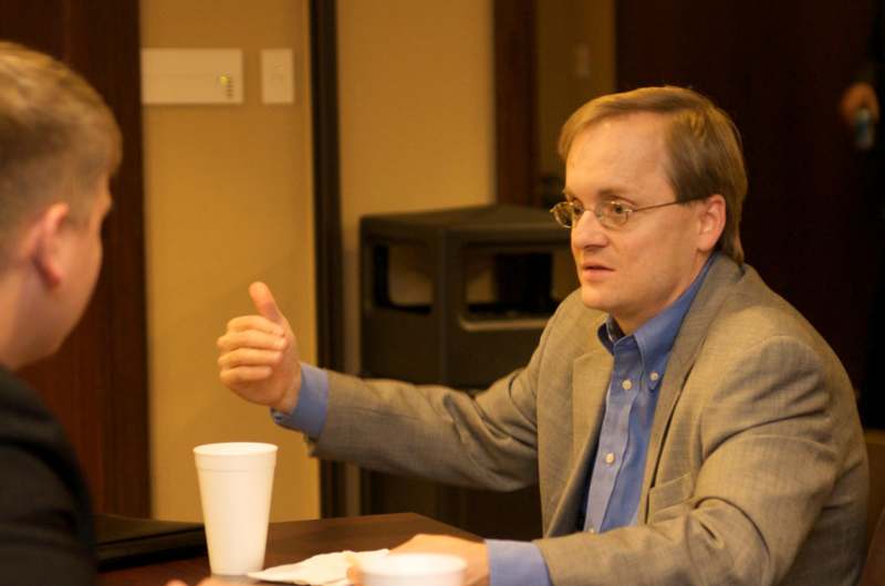a man sitting at a table with a cup and a thumb up
