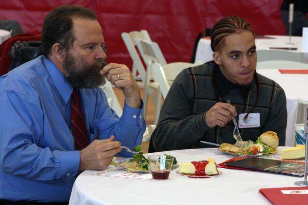 a man eating a meal with a man in a blue shirt