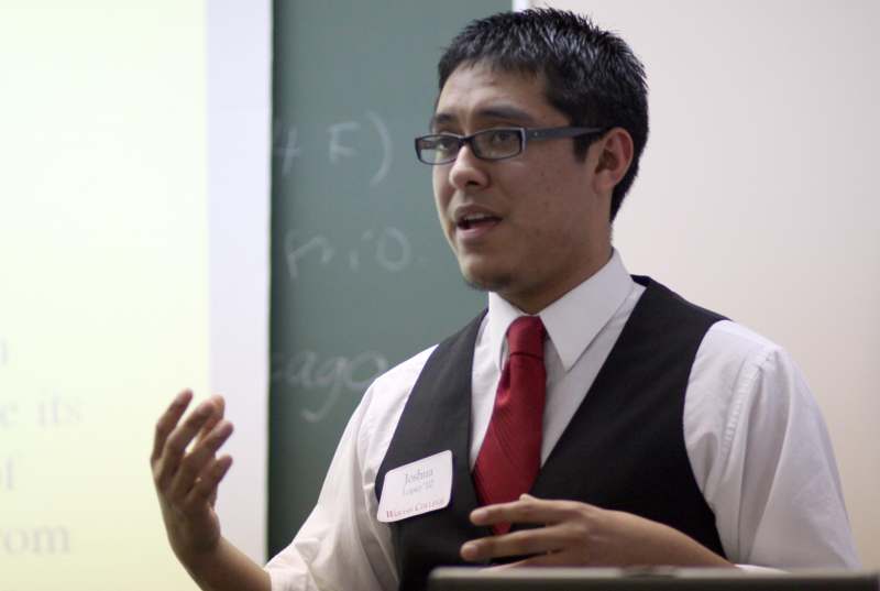 a man in a vest and tie speaking in front of a chalkboard