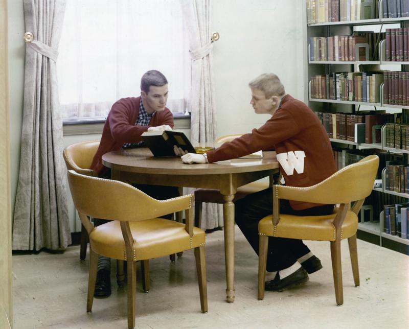 two men sitting at a table reading a book