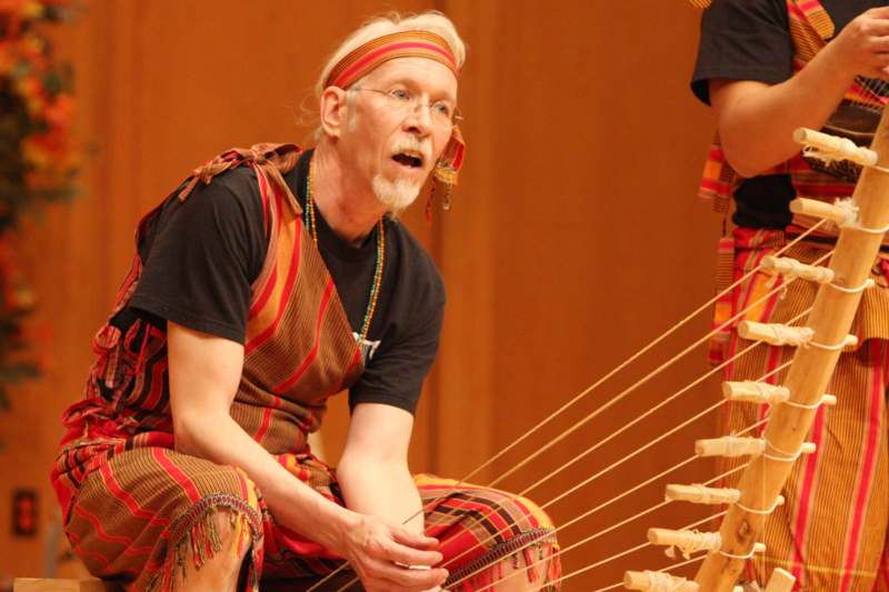 a man wearing a headband and a striped headband sitting on a wooden instrument